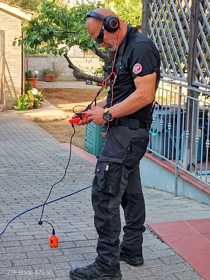 Operatore PRO-PIPE con cuffie e geofono appoggiato sulla pavimentazione durante la ricerca della perdita