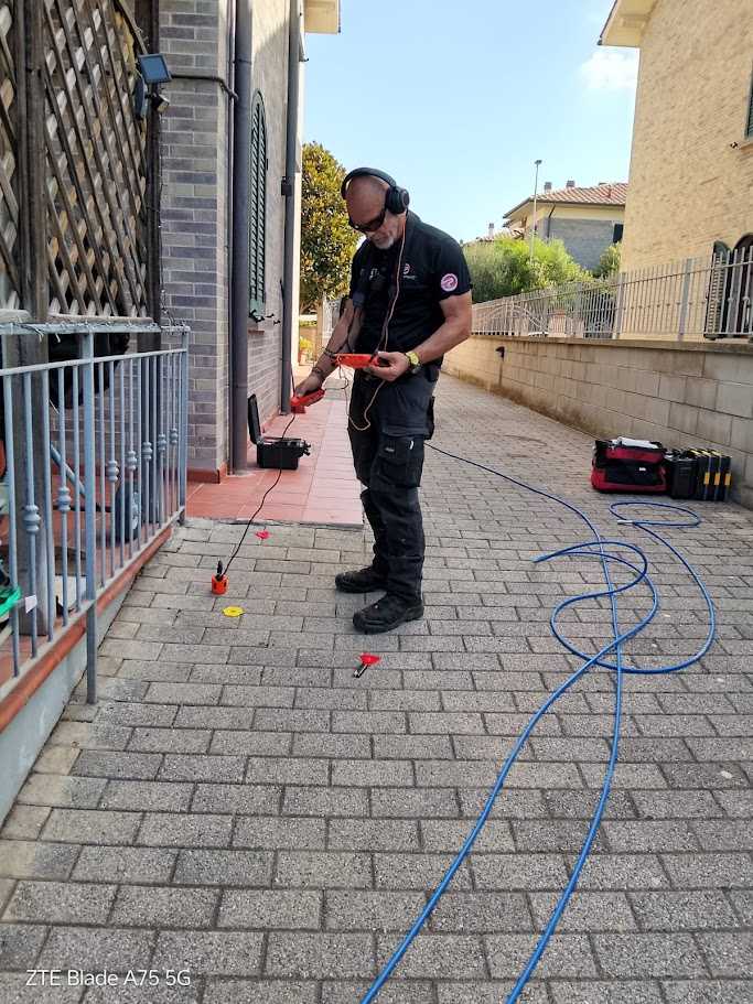 Operatore con cuffie e geofono sulla pavimentazione accanto ai contrassegni dei punti di verifica